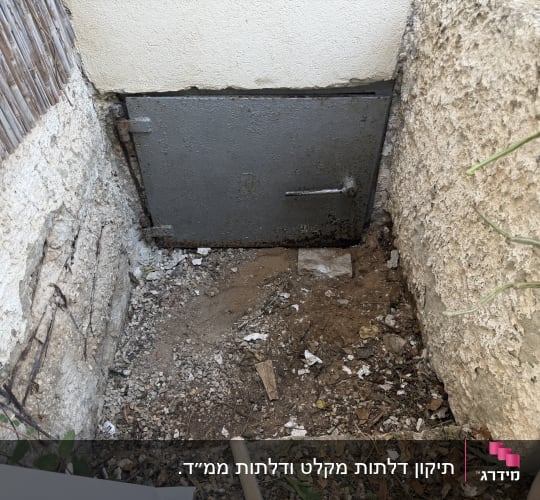 דלת מתכת ישנה בקיר חיצוני עם אדמה מסביב